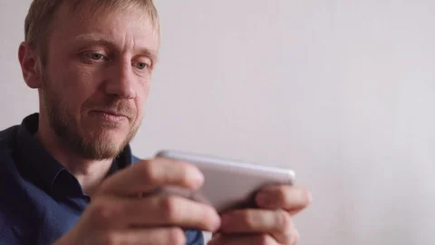Young man with a beard plays the game on his phone Stock Footage 128298496