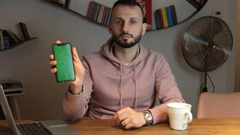 Young man with beard show green screen of the smatphone looking at the camera. Stock Footage 170963501