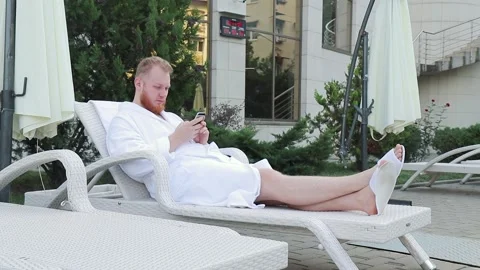 Young man with beard sits by the hotel pool on vacation with phone in his hands Stock Footage 147093545