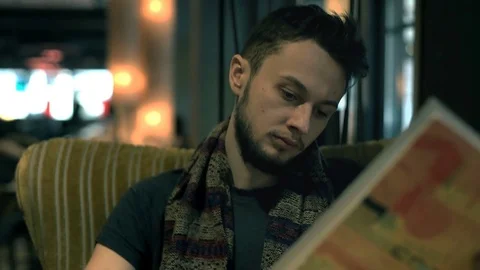 Young man with beard sitting on the armchair in the dark cafe and reading menu Stock-Footage 73105237