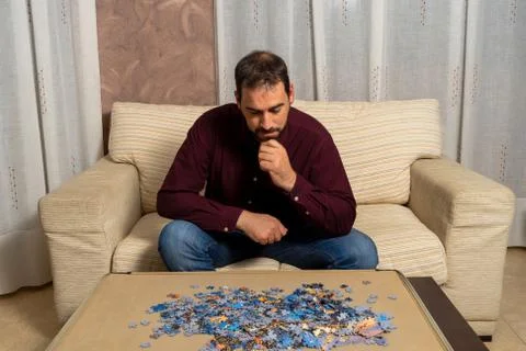 Young man with beard sitting on the couch at home doing puzzle Stock Photos