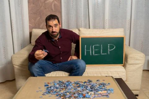 Young man with beard sitting on the couch at home doing puzzle Stock Photos