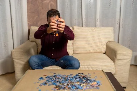 Young man with beard sitting on the couch at home doing puzzle Stock Photos