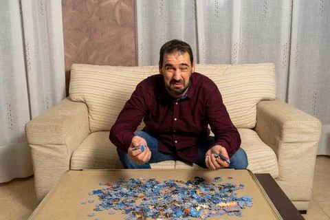 Young man with beard sitting on the couch at home doing puzzle Stock Photos