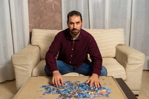 Young man with beard sitting on the couch at home doing puzzle Stock Photos