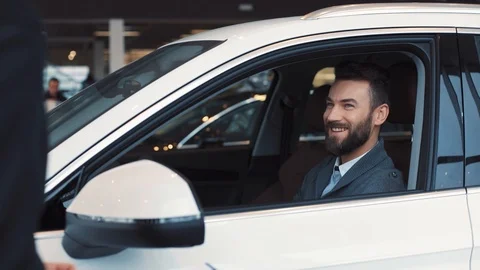 Young man with beard sitting in new white car. Guy laughing and thanking vendor Stock Footage 86175235