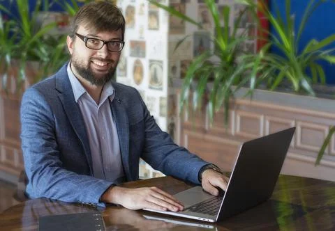 Young man with beard sitting at the table and using laptop Stock Photos