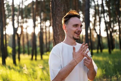 Young man with a beard smiling and gesturing in a sunlit forest Stock Photos