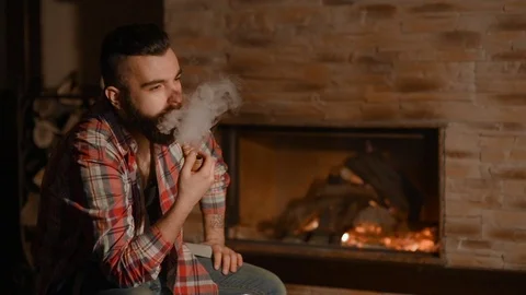 A young man with a beard smokes a pipe in a wooden house 動画素材 72465496