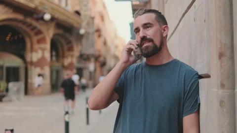 Young man with beard is talking on cellphone on the background of the old city Stock Footage 226898485