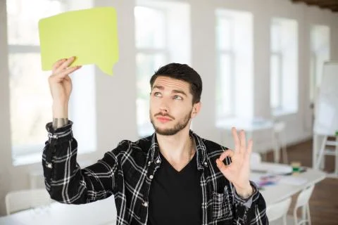 Young man with beard thoughtfully looking on green paper in cloud shape in hand Stock Photos