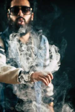 Young man with beard throwing a cloud of steam. Black background. Vaping an Stock Photos