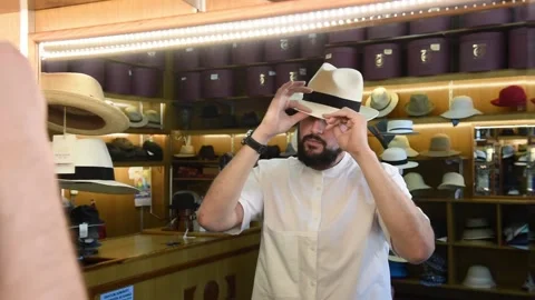 Young man with a beard trying on a hat in front of a mirror in a hat shop. Stock-Footage 131326082