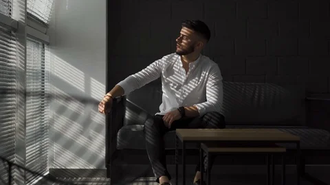 Young man with a beard turning his head and look at window and thinking 스톡 동영상 113607924