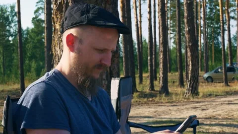 A young man with a beard on vacation in the forest is attentively leafing Stock Footage 158578812