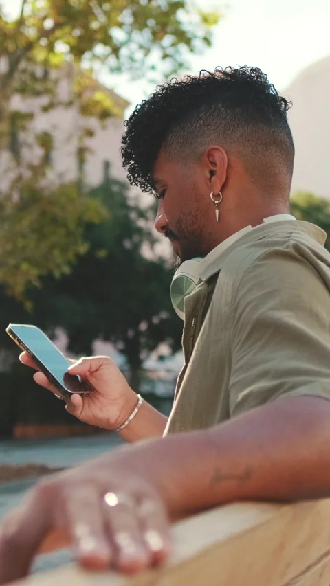 Young man with beard wearing an olive-colored shirt with headphones sits on Stock Footage 226859984