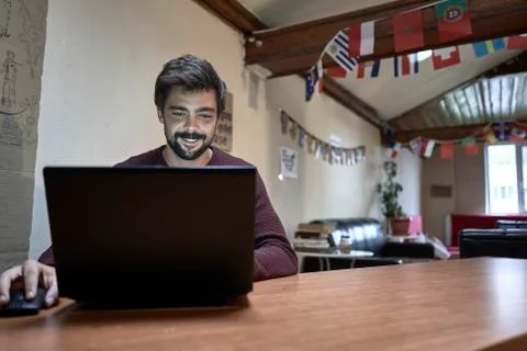 Young man with beard working with his lap top in a desk of a hostel Stock Photos