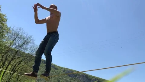 A young man with a beautiful torso is walking along a slackline. Stock Footage 108105639