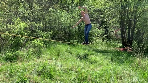 A young man with a beautiful torso is walking along a slackline. Stock Footage 108105665