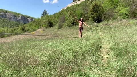A young man with a beautiful torso is walking along a slackline. Stock Footage 108105878