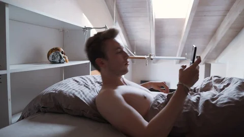 Young man in bed grabbing his phone and looking at the screen, 4K Stock Footage 129613877