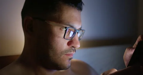 Young man in bed looks at the screen of his smartphone. Video stock 154324865