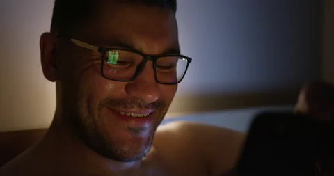 Young man in bed looks at the screen of his smartphone. Video stock 154324951