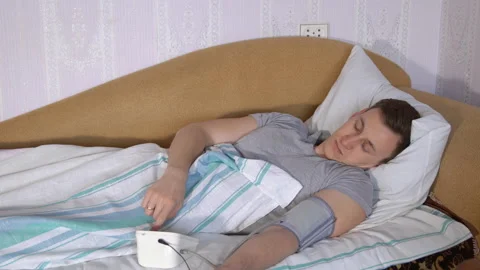 Young man in bed measures pressure by an electronic tonometer 스톡 동영상 90525446