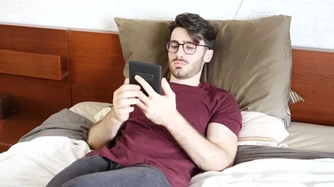 Young man on bed reading with ebook reader Video stock 78621621