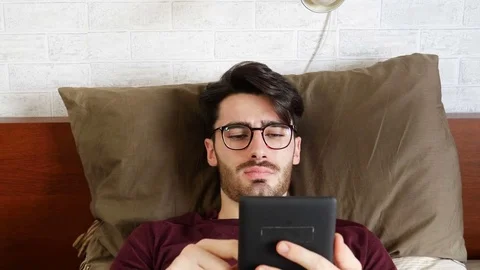 Young man on bed reading with ebook reader Stock Footage