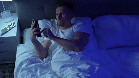 Young man in bed using smartphone to surf the internet at night. Insomnia a.. Stock Footage 289563033