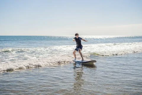 Young man, beginner Surfer learns to surf on a sea foam on the Bali island Stock Photos