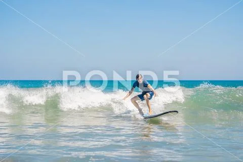 Young man, beginner Surfer learns to surf on a sea foam on the Bali island Stock Photos