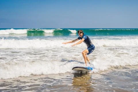 Young man, beginner Surfer learns to surf on a sea foam on the Bali island Stock Photos