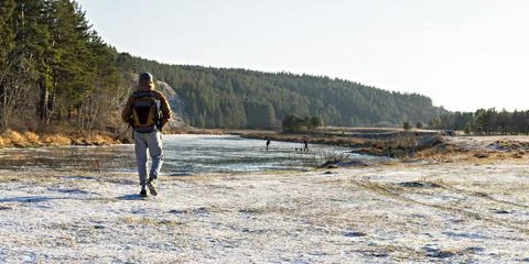 Young man from behind with a backpack walking by the river covered with ice Stock Photos