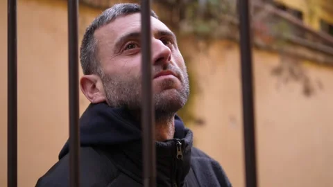 Young man behind gate looking up reflecting on life situation Stock Footage 332418001