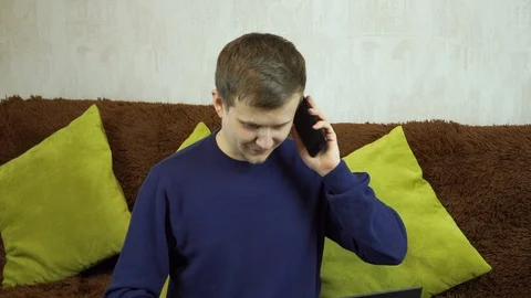 Young man behind laptop talking on mobile Stock Footage 99401709