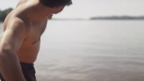 A young man from behind skipping a rock on the shore of a lake Stock Footage 116755409