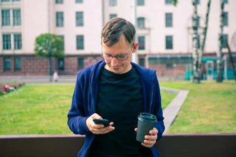 Young man on bench is drinking coffee in summer park Stock Photos