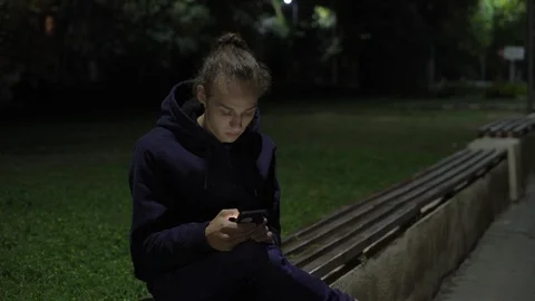 Young man on the bench scrolling feed on smartphone at night, 4k Vidéo 98878585