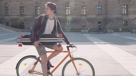 A young man on a bicycle is going to practice skateboarding Good sunny weather Stock Footage