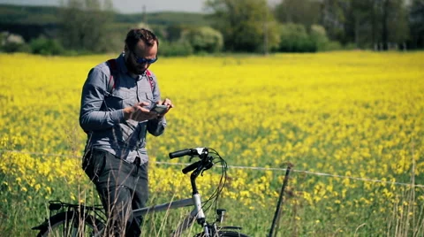 Young man on the bike checking direction on smartphone in the rape seed field HD Видео 49976962