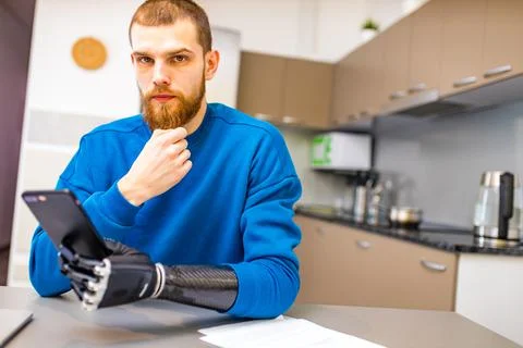 Young man with bionic hand hold smartphone while sitting indoors home kitchen Stock Photos