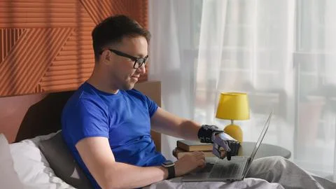 Young man with bionic prosthesis working on a laptop lying in bed at home Stock Photos