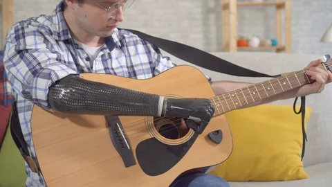 Young man with a bionic prosthetic arm plays an guitar Stock Footage 119412902