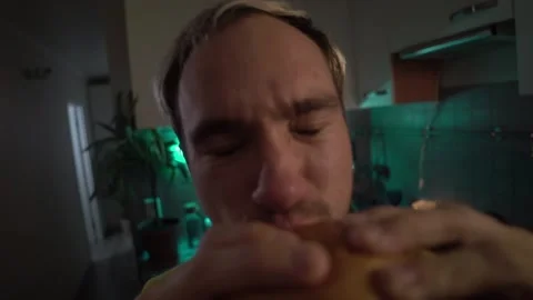 Young man bites fun at the burger in the kitchen Stock Footage 142393318