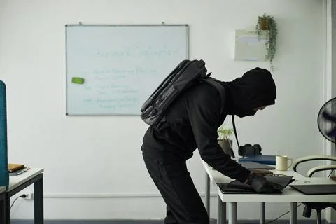 Young Man in Black, with Backpack Stealing Laptop in Office Stock Photos