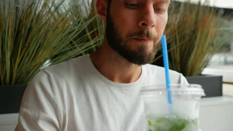 Young man with black beard drinks mojito at food court Stock Footage 137810143