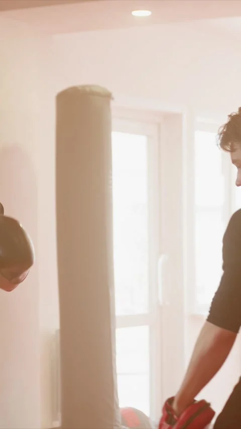 Young man in black boxing gloves practices aggressive punches toward red focus Stock Footage 343081911