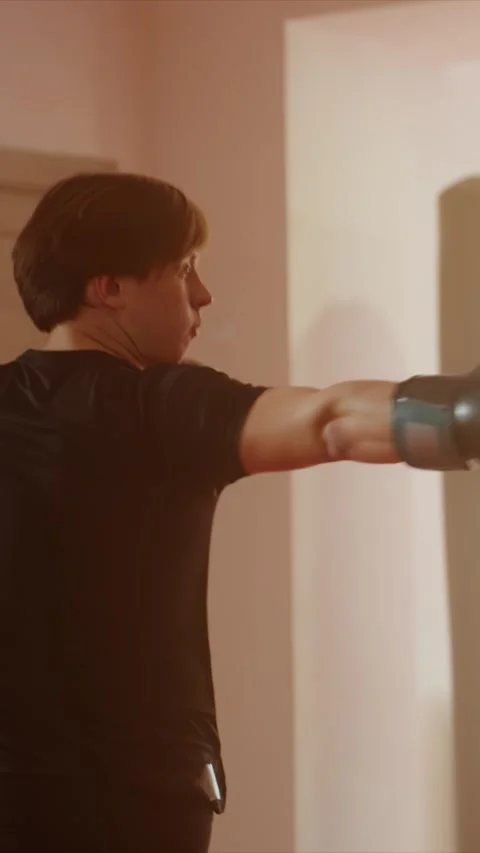 Young man in black boxing gloves practices punches and stances indoors with Stock Footage 346242026